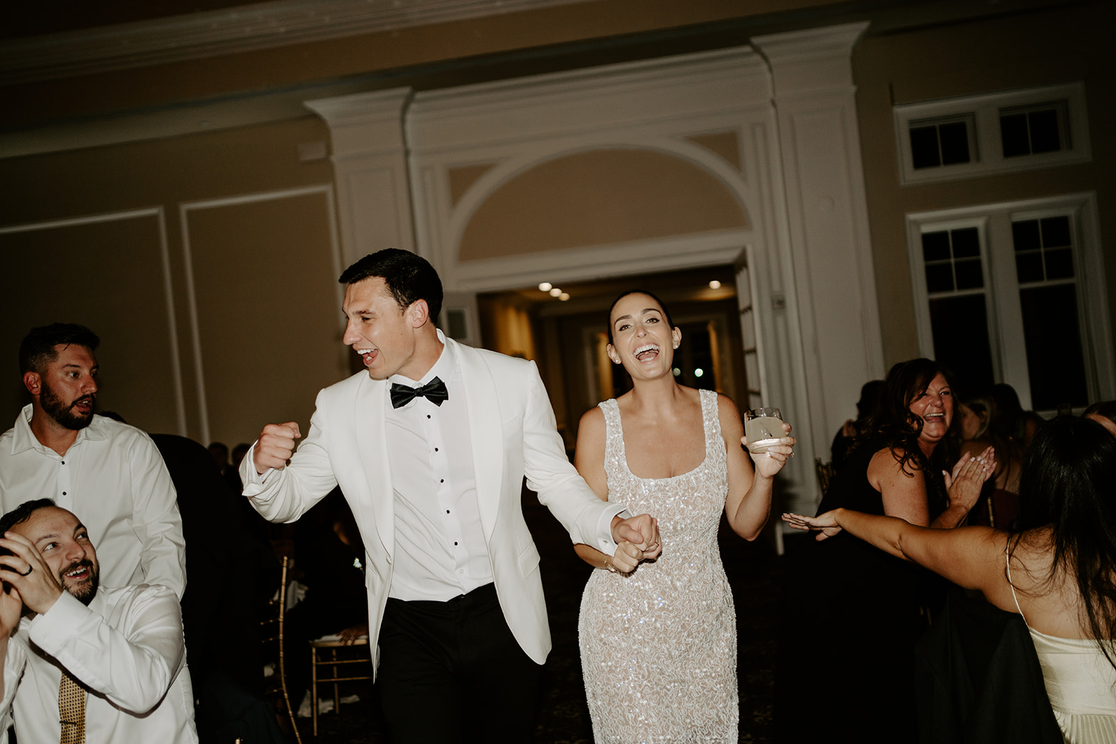 Newlyweds in reception outfit changes dancing hand-in-hand with joyful laughter on the dance floor.